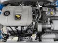 An overhead view of a 2021 Kia Forte engine with a gray cover labeled DOHC 18V and various components including tubes a battery and a coolant reservoir