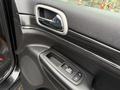 Interior door panel of a 2019 Jeep Grand Cherokee featuring control buttons for windows and door locks with a sleek metallic handle and textured black material