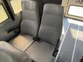 Two grey seats with vertical ribbed upholstery positioned in a bus interior with seatbelts attached