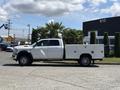 A 2021 RAM 5500 crew cab truck with a white utility bed and single rear wheels parked on a surface with palm trees nearby