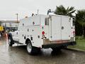 A 2015 Ford F-450 truck with a white utility body featuring tool compartments and safety lights on the rear
