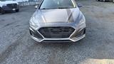A 2018 Hyundai Sonata with a sleek silver exterior and a prominent front grille is parked on a gravel surface