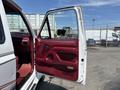A 1995 Ford F-250 with a white exterior and red interior features an open driver's door showcasing red upholstery and a black side mirror