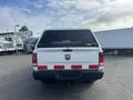 A 2012 RAM 2500 truck with a white body and a black Leer cap on the bed featuring a RAM logo and red and white stripes on the rear bumper