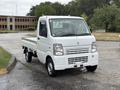 A white 2010 Suzuki Carry compact truck with a flatbed is parked in the foreground featuring a simple design and small dimensions