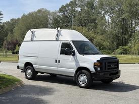 A white 2008 Ford Econoline van with a high roof and roof racks parked on a paved surface