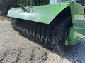 A close-up view of a green John Deere 1575 street sweeper with a large black bristle brush attachment in the foreground