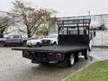 A 2015 Hino 195 flatbed truck with a black wooden bed and a metal mesh backrest positioned in a parking lot