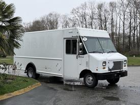 A white 2012 Ford Econoline box truck with a flat front and side doors is parked on a slight incline with visible wheels and a clear windshield