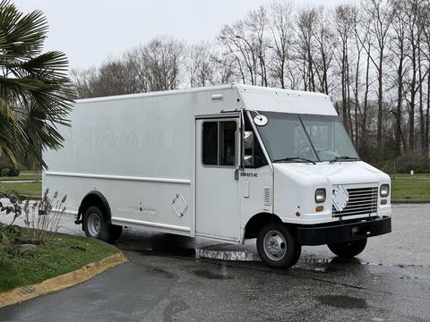 A white 2012 Ford Econoline box truck with a flat front and side doors is parked on a slight incline with visible wheels and a clear windshield