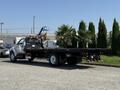 A 2008 Ford F-750 flatbed truck with a black bed and white cab is parked, showcasing its long flatbed and rear lights