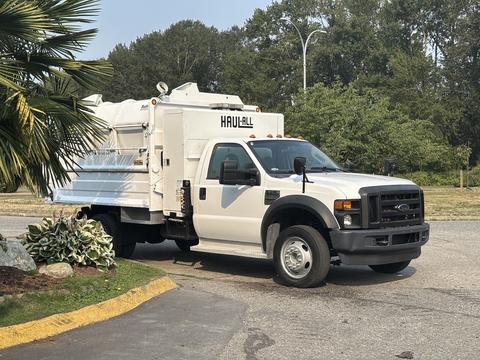 A white 2009 Ford F-550 truck with a large rear container designed for hauling materials