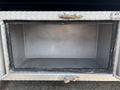 An empty storage compartment of a 2020 Peterbilt 330 with a diamond plate exterior and a metal latch for securing the door