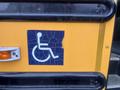 A cracked blue and white wheelchair symbol sticker on a yellow surface attached to a bus