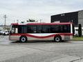 A 2016 Grande West Vicinity bus with a red and white design is parked, showcasing its side profile and large windows