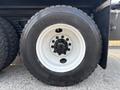 A close-up of a large Freightliner truck tire mounted on a wheel with a white rim and a black tread pattern