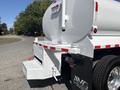A 2014 Freightliner M2 106 tank truck featuring a white tank with red stripes and chrome wheels parked on a road
