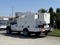 A 2008 Ford F-550 utility truck with a white body featuring storage compartments and an elevated bucket lift on the side