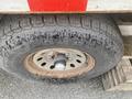 A close-up of a tire mounted on a wheel hub showing a tread pattern with visible dirt and wear on a rusted rim