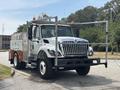 A 2012 International 7300 Workstar truck with a silver body and orange lights equipped with a utility bed and a mounted ladder rack on top
