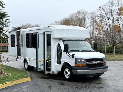 A white 2015 Chevrolet Express with an extended body and wheelchair lift doors open on the side is parked at an angle