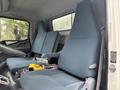 Interior of a 2015 Mitsubishi Fuso FE160 featuring two blue fabric seats and a central console with controls and a yellow tool on it