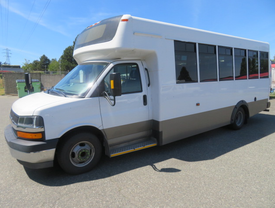 A 2020 Chevrolet Express bus with a white exterior, large windows, and a low entrance step is parked on a paved surface
