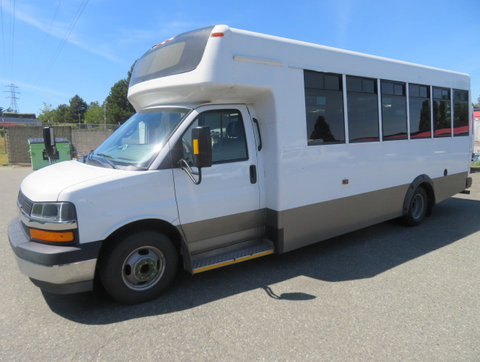 A 2020 Chevrolet Express bus with a white exterior, large windows, and a low entrance step is parked on a paved surface