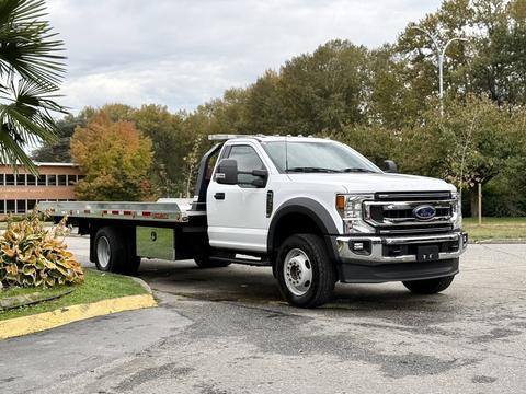 A white 2022 Ford F600 flatbed truck with a cab and a large flatbed cargo area is parked at an angle
