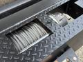 A spool of thick steel cable is visible inside a metal compartment mounted on a platform with a textured surface