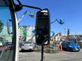 A 2022 Isuzu NRR truck side mirror reflects the surrounding construction equipment and vehicles parked nearby
