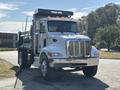 A 2015 Peterbilt 337 dump truck with a silver cab and chrome grille featuring orange lights on top and a green dump bed at the back