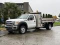 A white 2015 Ford F-450 with a flatbed and utility box attached parked on a wet surface