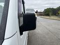 A white 2010 Suzuki Carry with a side mirror visible in the foreground and a blurred vehicle behind it