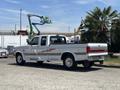 A 1995 Ford F-250 pickup truck in white with a red stripe featuring a double cab and chrome wheels parked outdoors