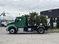 A green 2013 Kenworth T370 flatbed truck transporting several potted palm trees on the flatbed