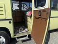 A 1976 GMC Motorhome with an open brown door showcasing a green and striped interior couch and a colorful blanket draped over it