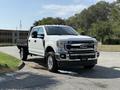 A white 2020 Ford F-350 SD truck with a flatbed and chrome accents is parked at an angle with its headlights on