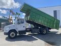 A 1997 Freightliner FL70 dump truck with a green cargo bed raised in the air for unloading