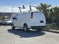 A 2019 GMC Savana van in white with a ladder rack on the roof parked on a lot with palm trees nearby