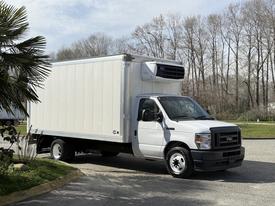A 2023 Ford E-450 truck with a white box cargo area and a cooling unit mounted on top parked on a driveway