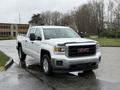 A white 2015 GMC Sierra 1500 pickup truck parked in a lot with a gray sky above and trees in the background