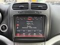 A 2013 Dodge Journey dashboard displaying a touchscreen interface with radio information and controls for player climate and settings