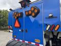 A 2013 International DuraStar 4300 featuring a blue body and multiple orange and red lights on the rear doors alongside a triangular hazard sign