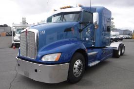A blue 2015 Kenworth T660 truck with a shiny chrome grille and headlights sits prominently in the foreground
