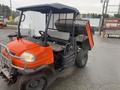 A 2010 Kubota RTV 900 off-road utility vehicle with an orange and black body featuring a dump bed and an enclosed cabin with a gray seat