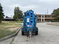 A blue Genie TZ-34/20 aerial lift with a raised platform and a trailer hitch positioned facing forward