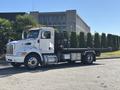A white 2020 Peterbilt 330 tow truck with a flatbed and side railings parked on a street