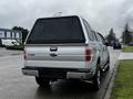 A silver 2014 Ford F-150 pickup truck with a camper shell on the bed parked along a roadway