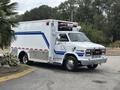 A 1994 GMC Vandura 3500 emergency vehicle with a white body and blue stripes equipped with lights on the roof and side doors